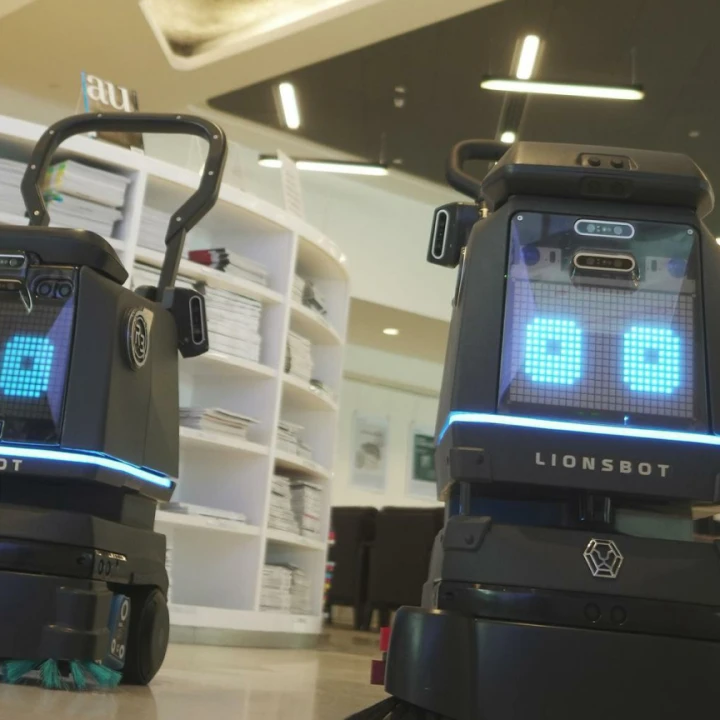 Robotvaskere med blå øyne og sort kropp som vasker et gulv i en butikk